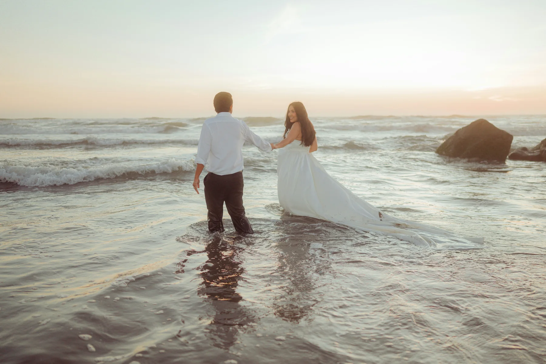 Wedding couple walking into the ocean at sunset