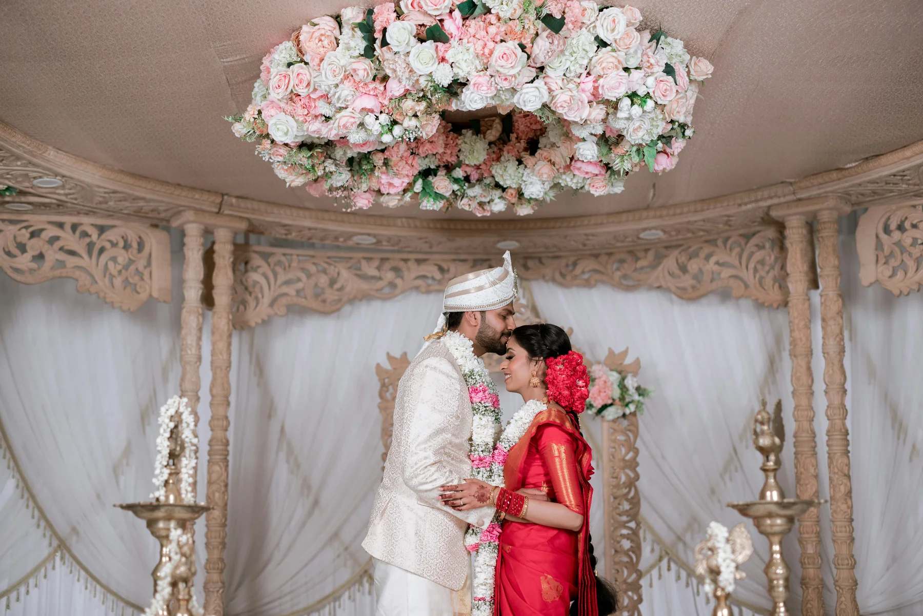 Indian bride and groom beneath a floral wedding mandap